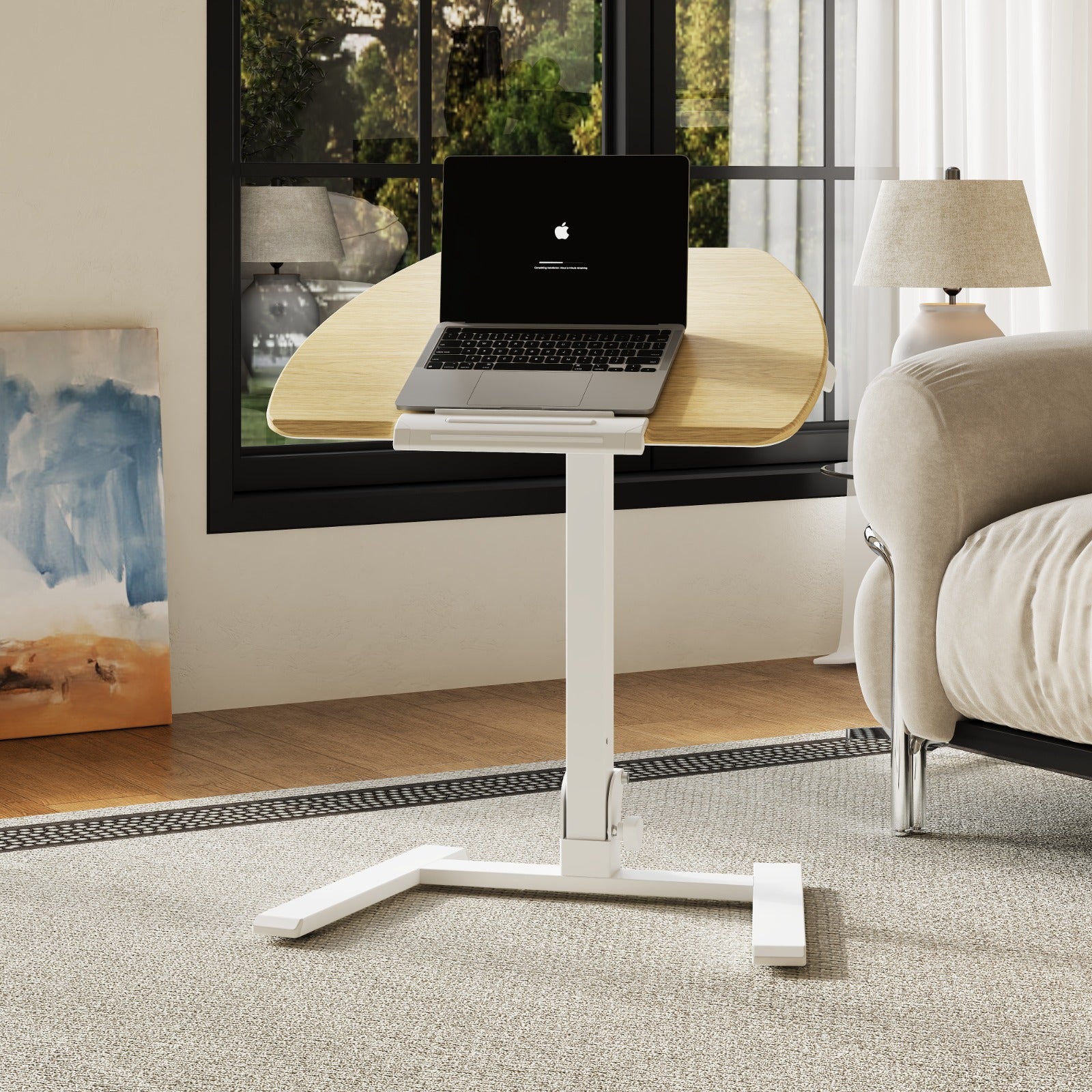 A modern white portable standing desk placed beside a leather sofa in a bright, minimalist living room, featuring a tilted laptop surface and ergonomic design.