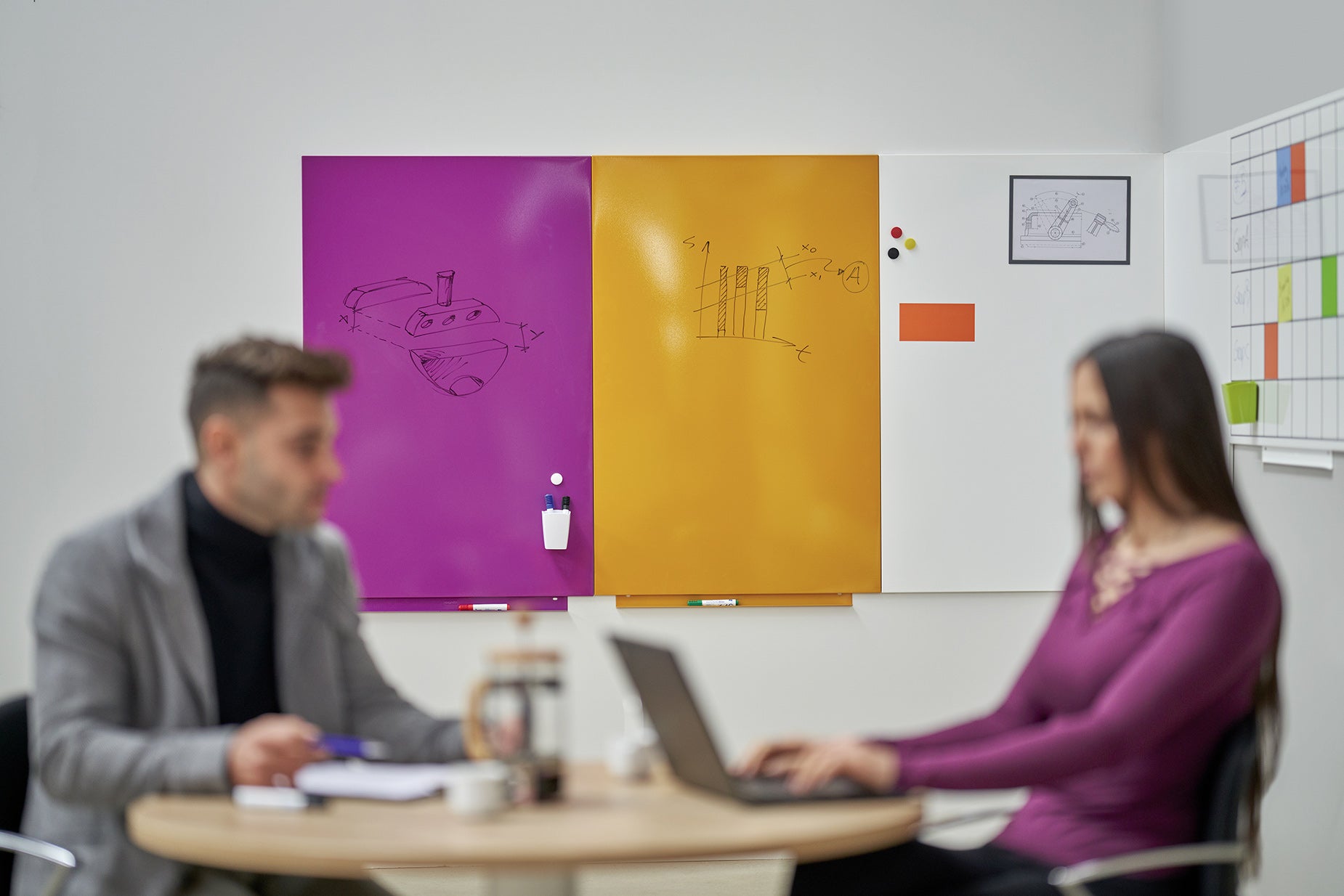 Two professionals brainstorming in front of a modular whiteboard system featuring vibrant purple, orange, and white panels β perfect for dynamic office collaboration.