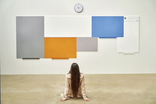 Woman sitting in front of a large modular whiteboard installation composed of colourful interconnected panels – ideal for creative planning, collaboration, and customisable workspace design.